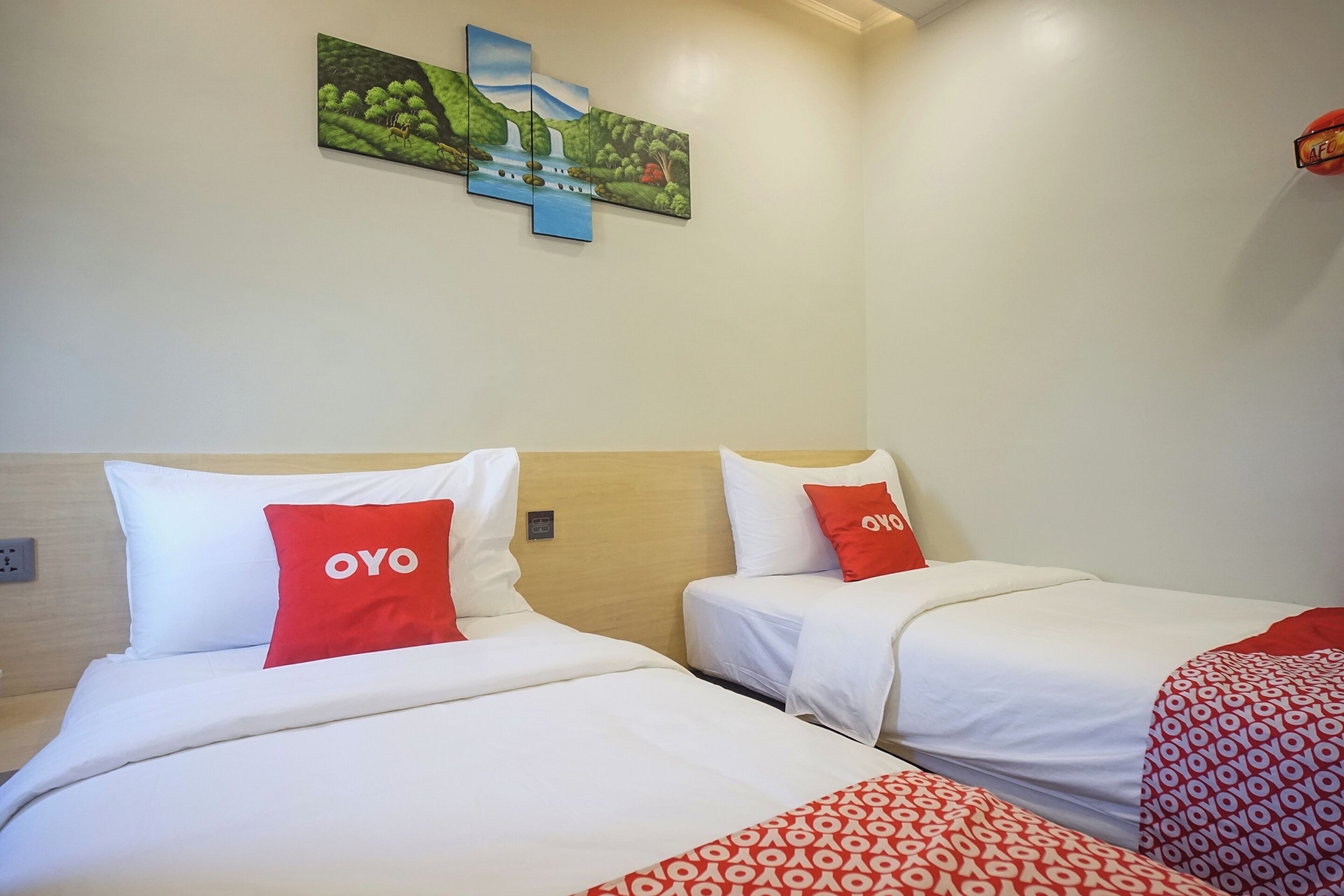 Ein Hotelzimmer mit zwei Betten, jeweils mit weißer Bettwäsche und roten Kissen. Über den Betten hängt ein Landschaftsbild.