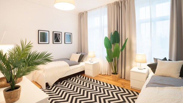 A modern bedroom with a bed, bedside tables, lamps, and a large window with curtains.