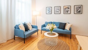 A modern living room with two blue sofas, a round coffee table with a vase of flowers, and a floor lamp.