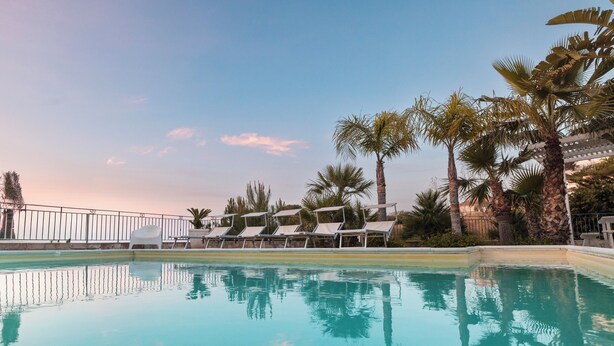 Una piscina con sillones de descanso y palmeras.