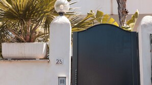 Pared blanca con una verja negra, una planta en maceta y un letrero con el número 25.