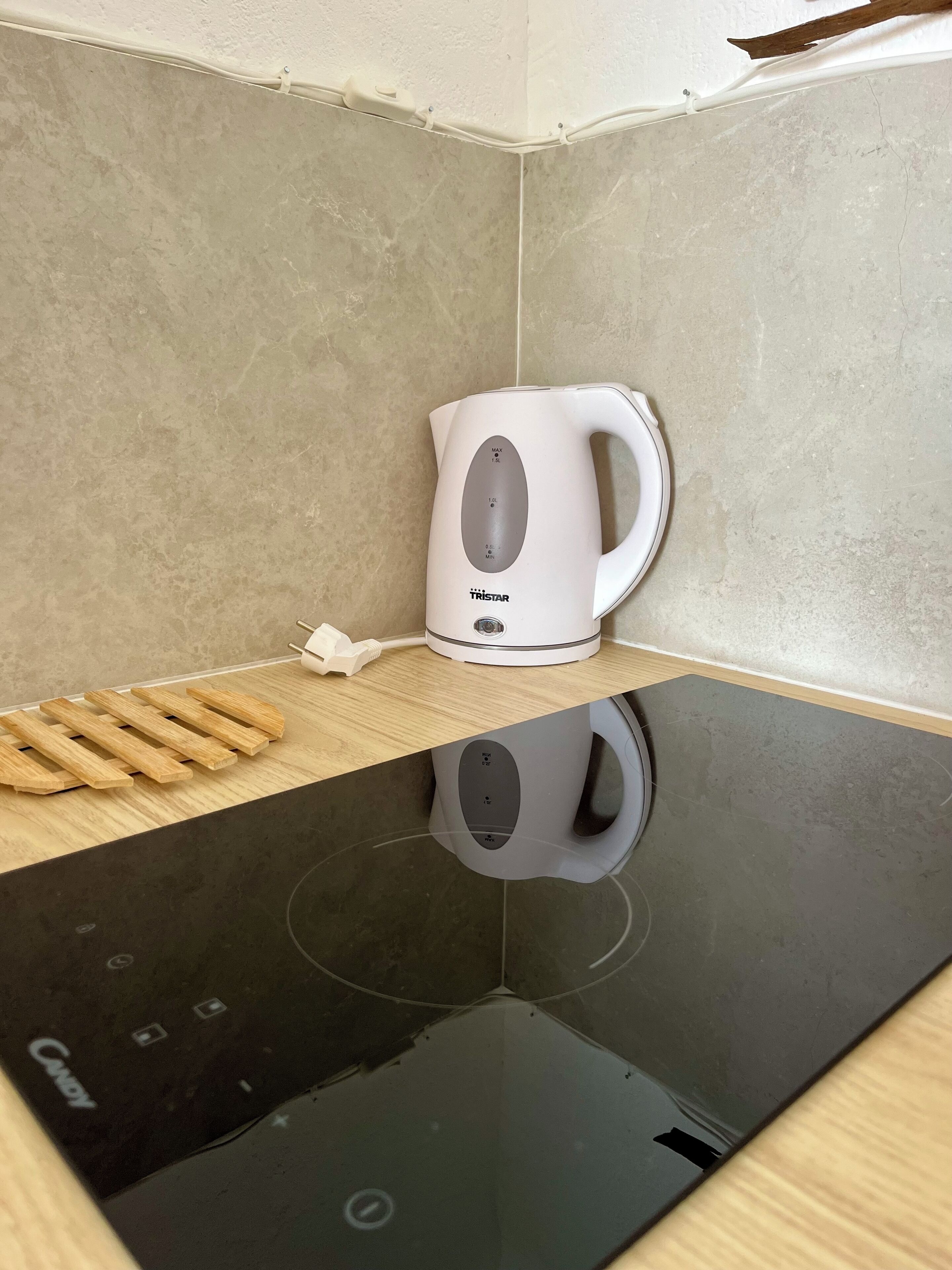 Una tetera eléctrica blanca sobre una encimera de madera con una cocina de inducción negra debajo.