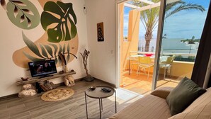 Una sala de estar moderna con un sofá grande, un televisor de pantalla plana y una zona de comedor con sillas amarillas.
