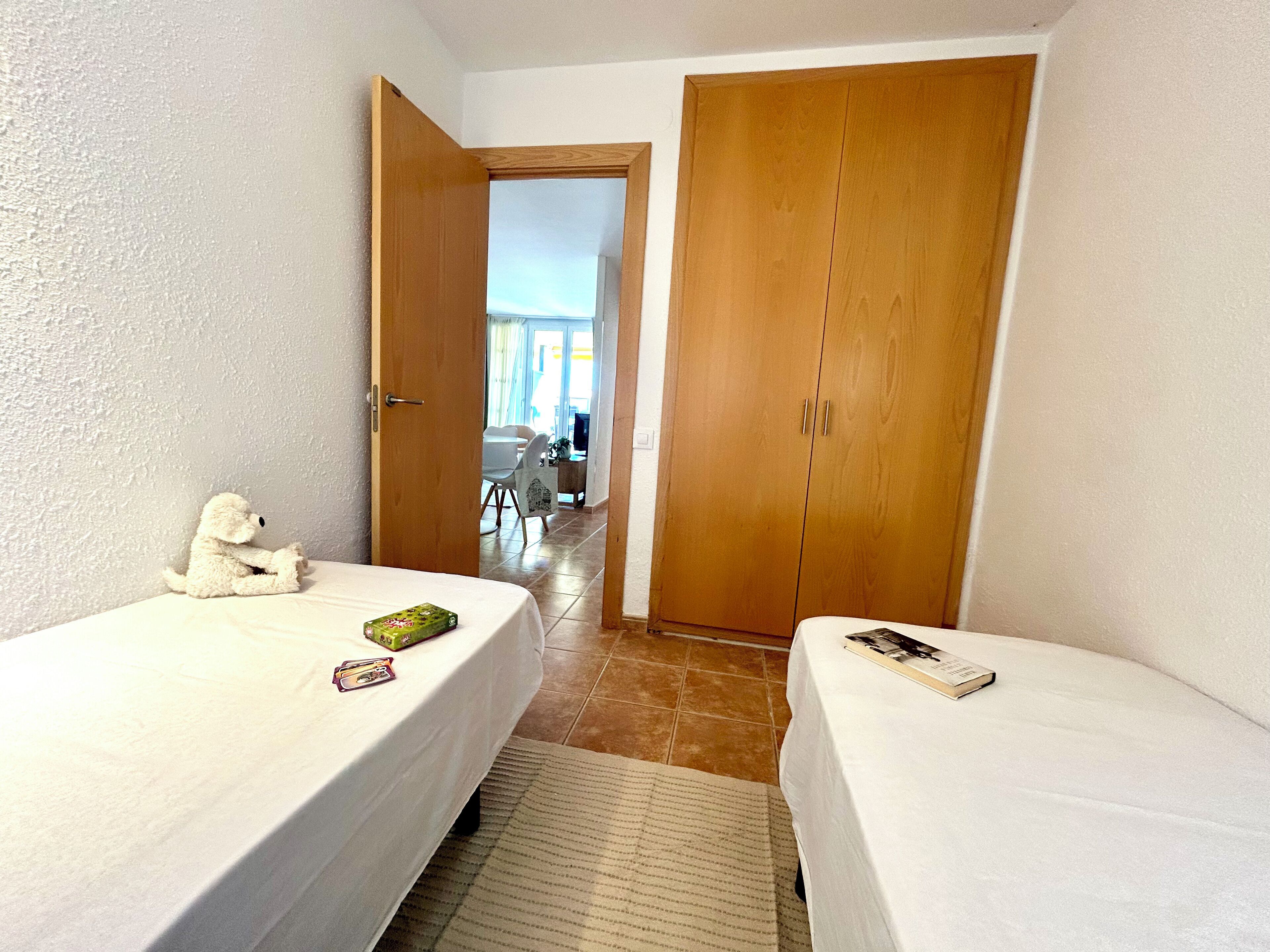 A room with two single beds, a wooden wardrobe, and a small white teddy bear on one bed.