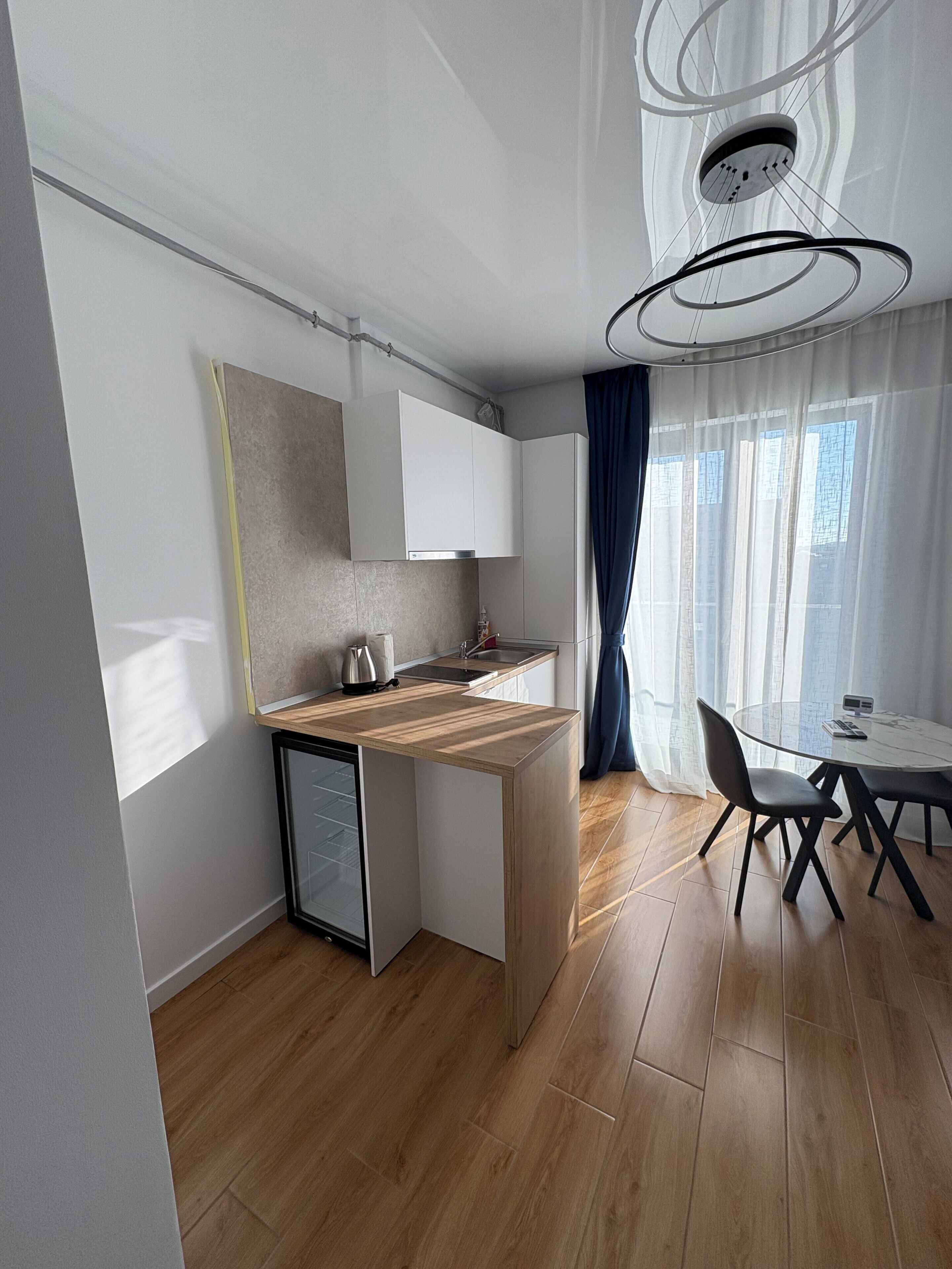 A modern kitchen with a built-in dishwasher, a small refrigerator, and a wooden countertop. There is a dining area with a round table and chairs.