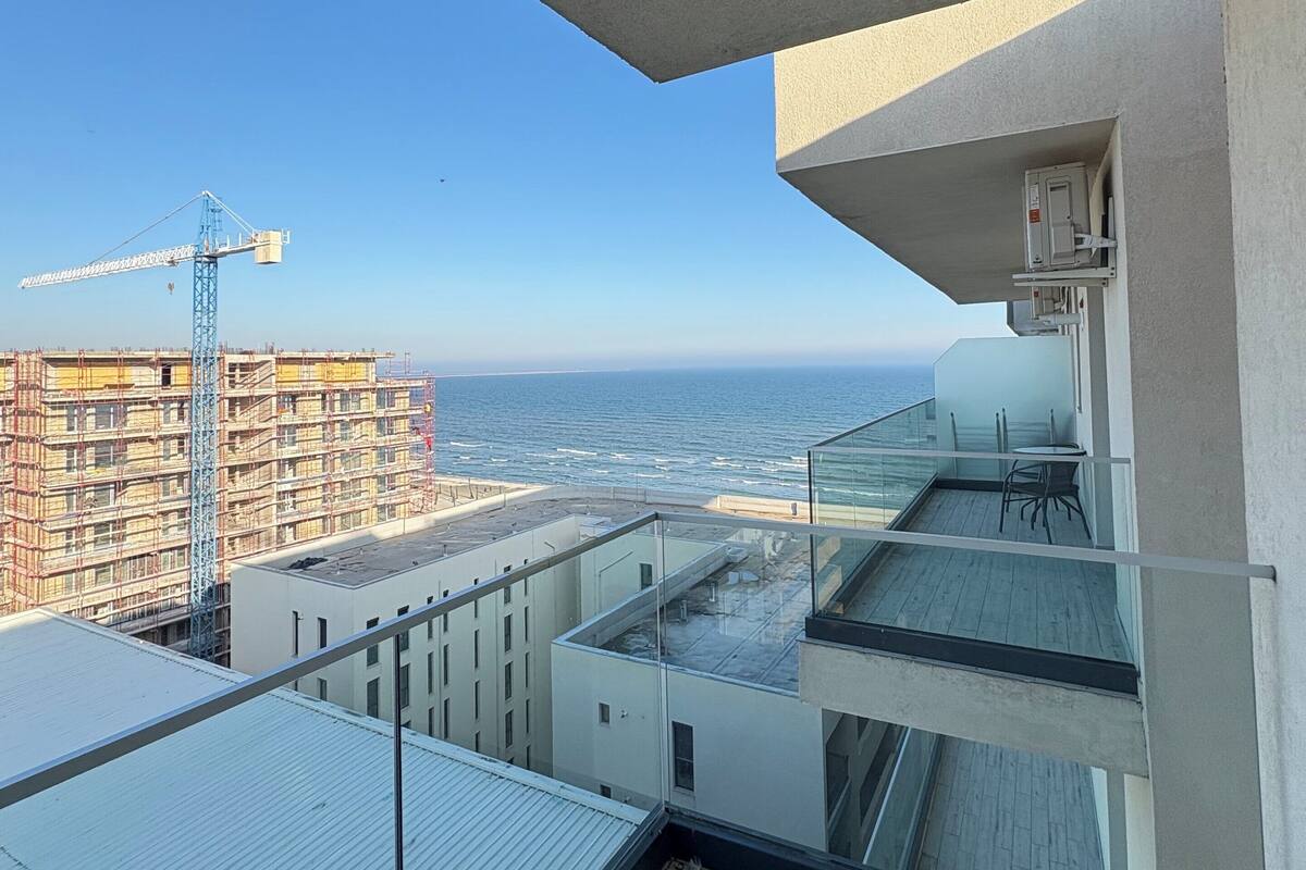A balcony with a view of the sea and construction cranes in the background.