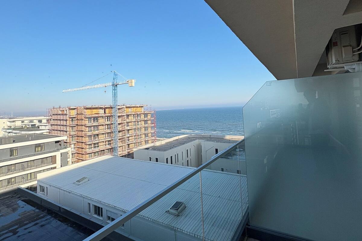 A high-rise building with a view of the ocean and construction cranes in the distance.