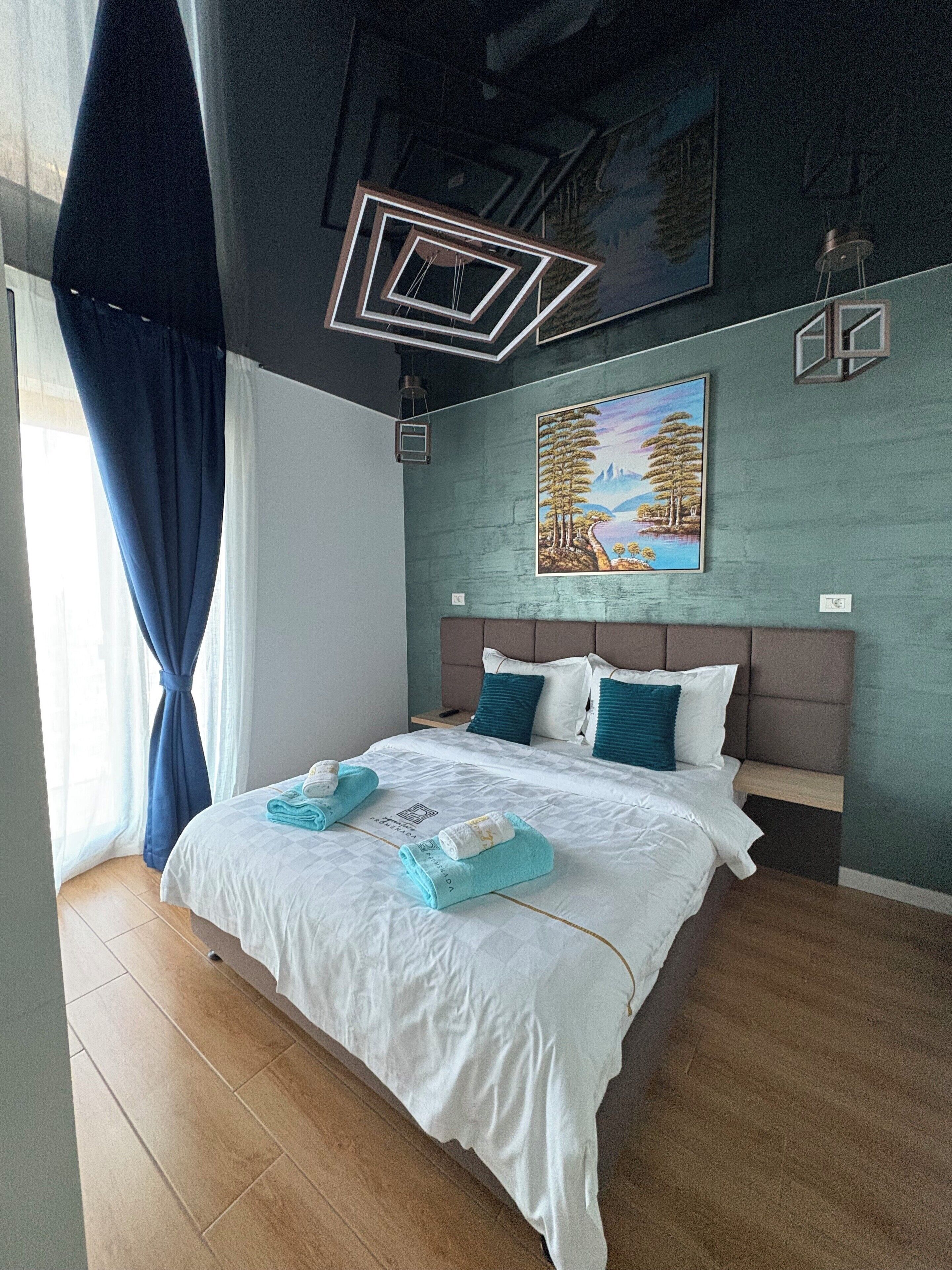 Una habitación de hotel moderna con una cama grande, un cuadro en la pared y una lámpara de techo original.