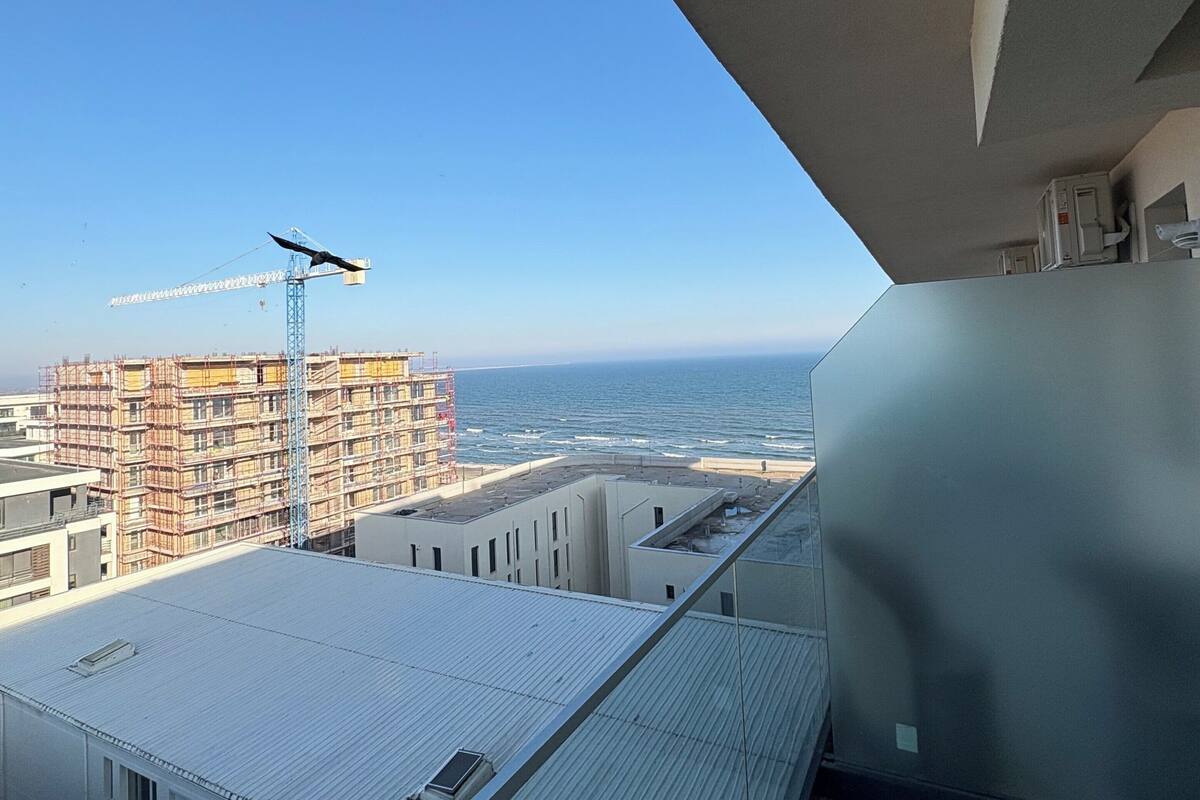 A high-rise building with a view of the ocean and a construction crane in the distance.