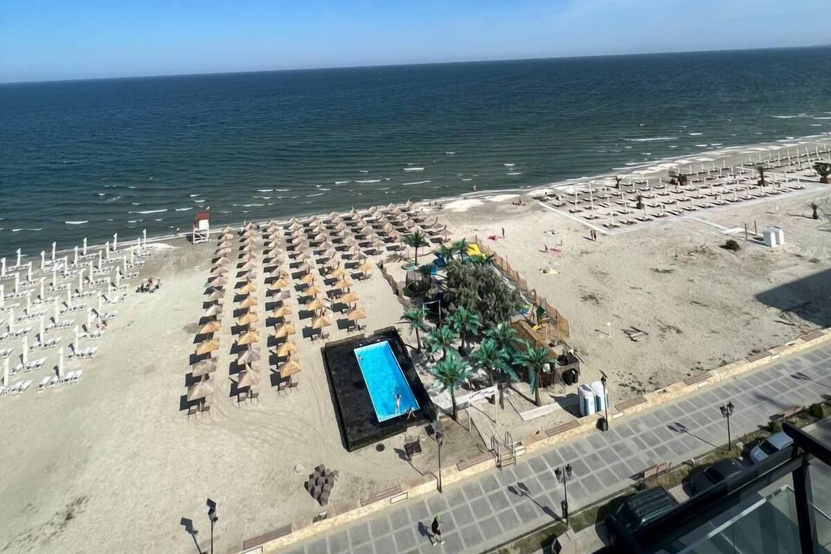 A beach with rows of sun loungers and a swimming pool.