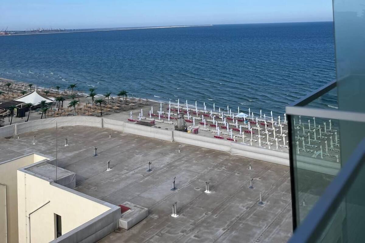 A view from a balcony overlooking a beach with umbrellas and lounge chairs, a clear sky, and a calm sea.