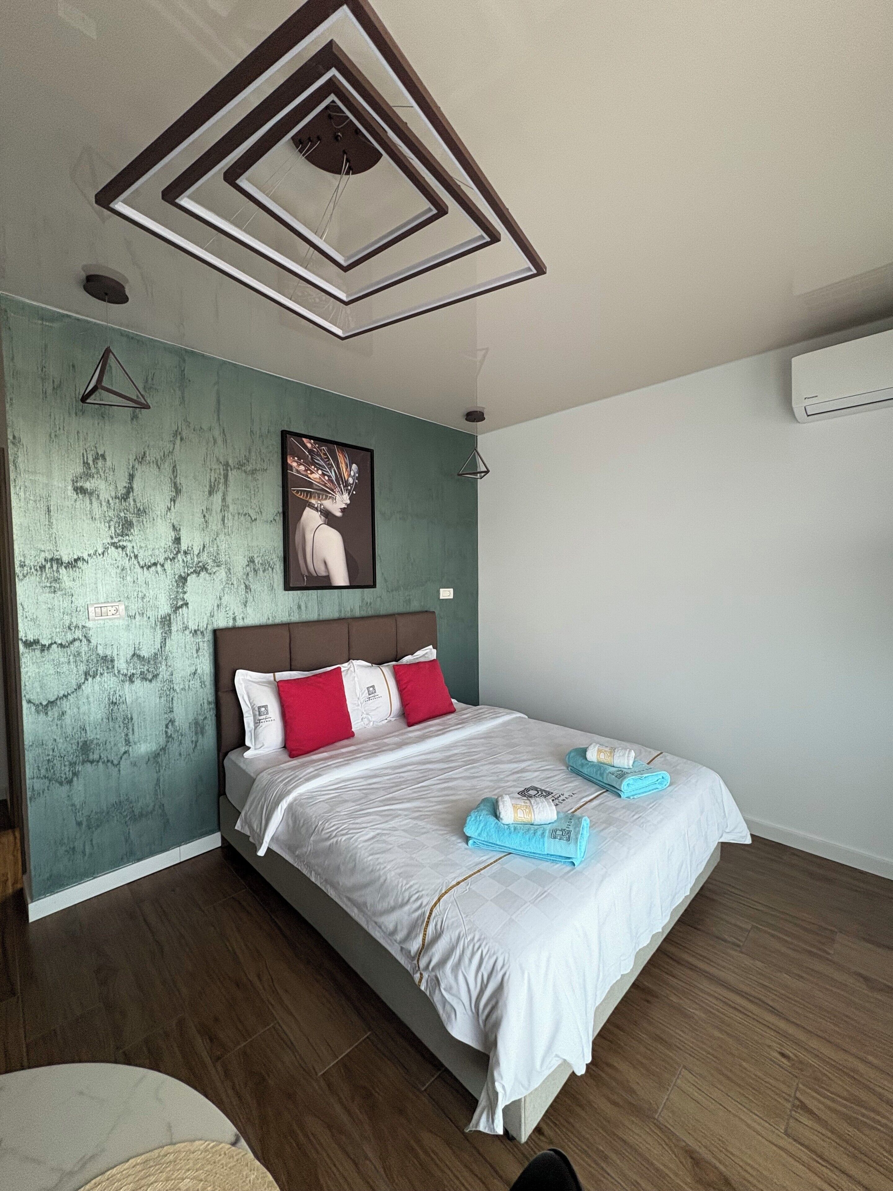 Ein modernes Schlafzimmer mit einem Bett, einem Gemälde und einem einzigartigen Deckenstil.