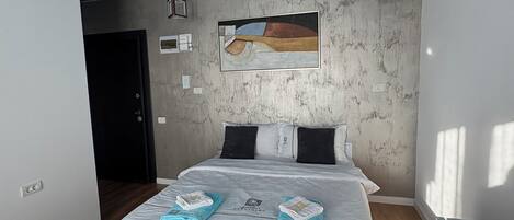 A modern bedroom with a large bed, a painting on the wall, and a unique ceiling design.
