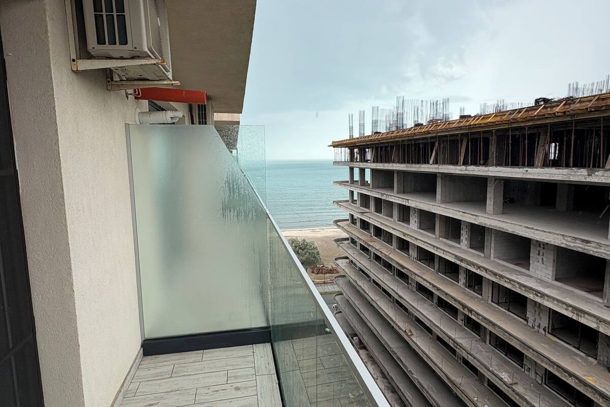 A balcony with a view of the sea, a construction site, and a building under construction.