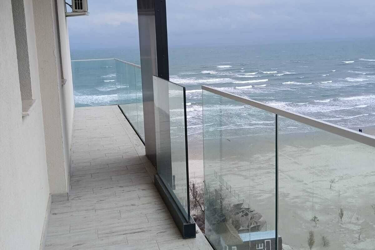 A balcony with a glass railing overlooking a beach and ocean.