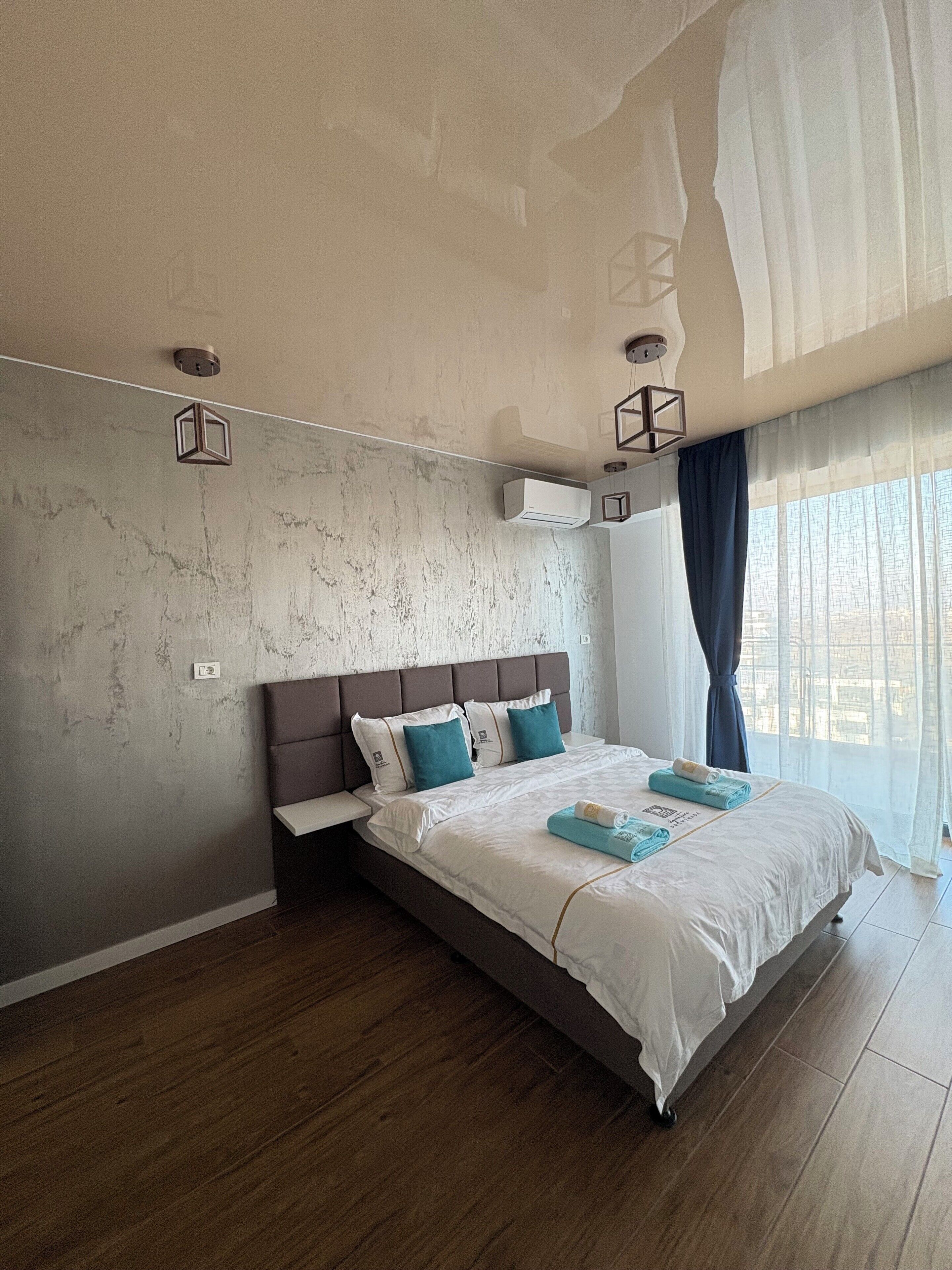 A modern bedroom with a large bed, a headboard, and a window with curtains.