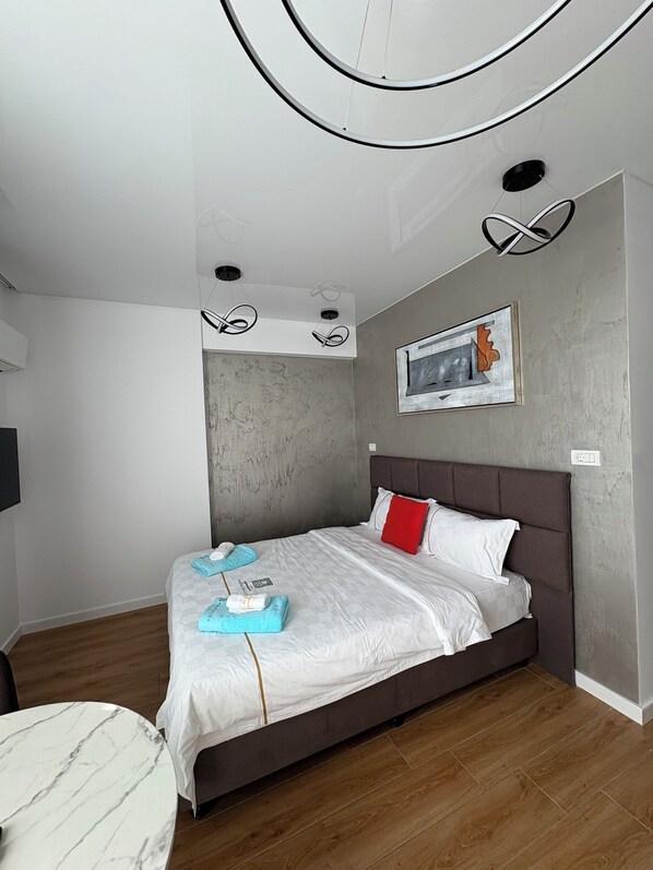 A modern hotel room with a large bed, a marble-topped table, and a grey textured wall. - Signature Promenada Hotel-Apartments (Navodari)