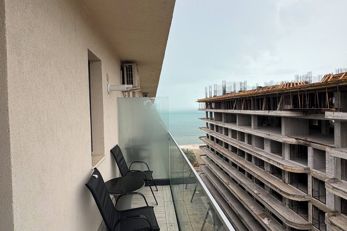 A balcony with a view of the sea, a glass railing, and a row of empty balconies.