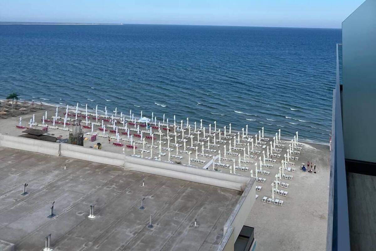 A view of a beach with rows of white umbrellas and lounge chairs, a clear blue sky, and the ocean in the background.