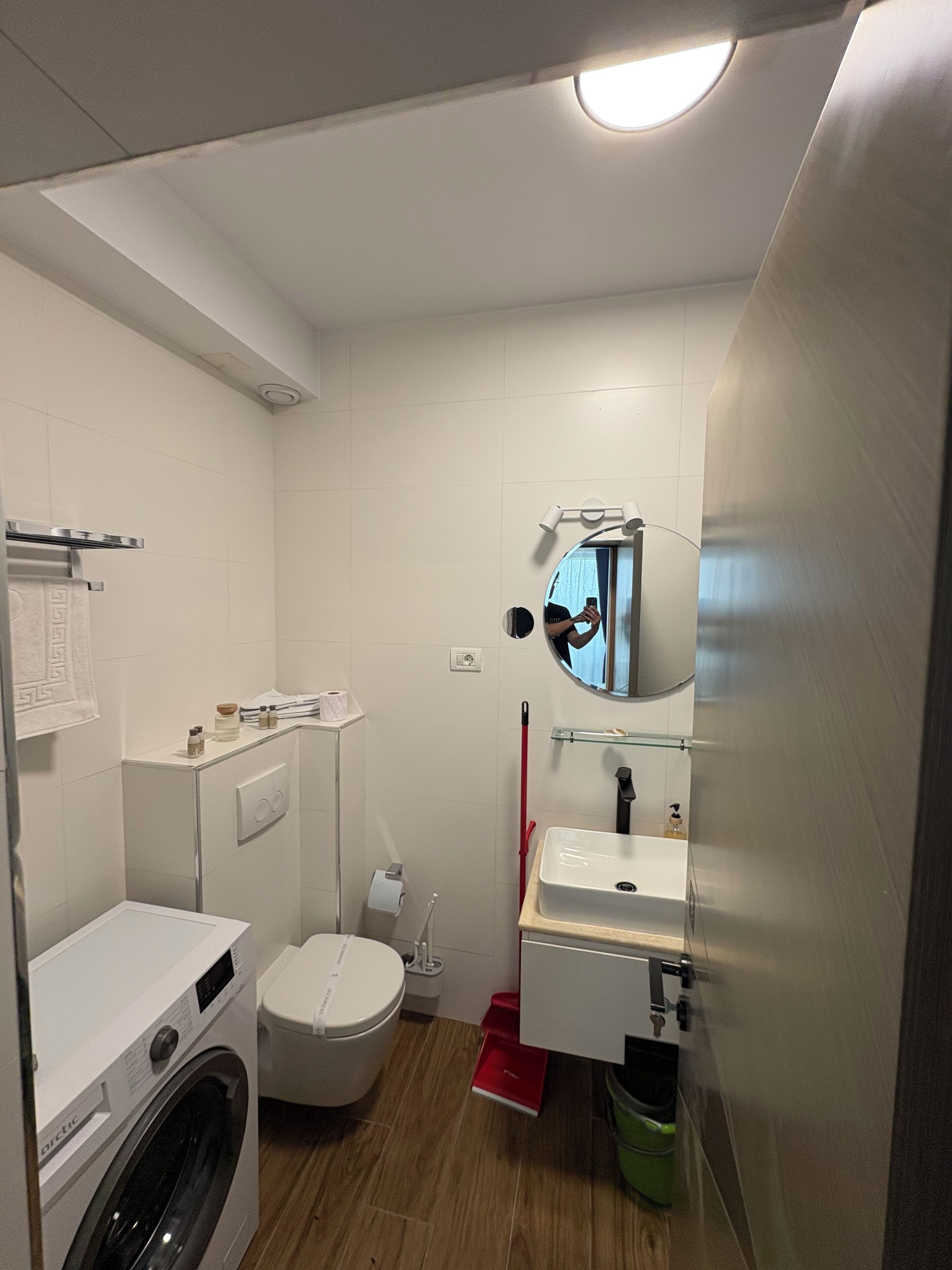 A compact bathroom with a washing machine, toilet, sink, and a mirror.