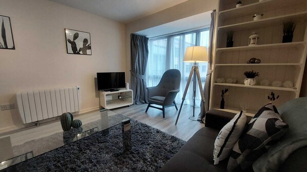 A modern living room with a sofa, a television, a chair, a lamp, and a bookshelf.