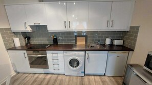 A compact kitchen with a built-in oven, a washing machine, and a coffee maker. - Modern 2BD @ Trinity College & Temple Bar (Dublin)