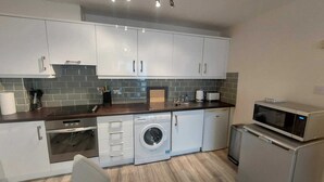 A compact kitchen with white cabinets, a washing machine, a microwave, and a toaster.