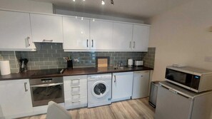 A compact kitchen with white cabinets, a washing machine, a microwave, and a toaster. - Modern 2BD @ Trinity College & Temple Bar (Dublin)