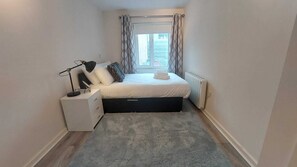 A small, neatly arranged bedroom with a bed, bedside table, lamp, and a radiator. - Modern 2BD @ Trinity College & Temple Bar (Dublin)