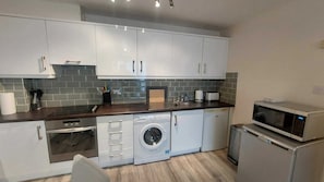 A compact kitchen with white cabinets, a washing machine, a microwave, and a toaster.