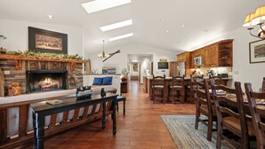 A spacious living room with a fireplace, wooden furniture, and a view into the kitchen.