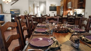 A dining table set with purple plates, clear glasses, and a centerpiece of pinecones and a ceramic bird.