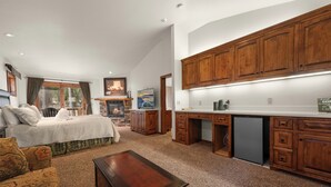 A spacious living area with a large bed, a wooden coffee table, and a kitchen with wooden cabinets and a refrigerator.