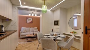 Un espace repas moderne avec une table ronde dressée pour quatre personnes, un canapé en arrière-plan et un coin cuisine équipé d’une machine à café.