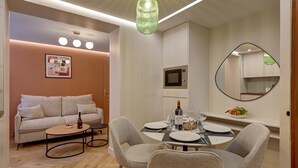 Un salon moderne avec un canapé, une table à manger pour quatre personnes et un coin cuisine équipé d’un four à micro-ondes et d’un grand miroir.
