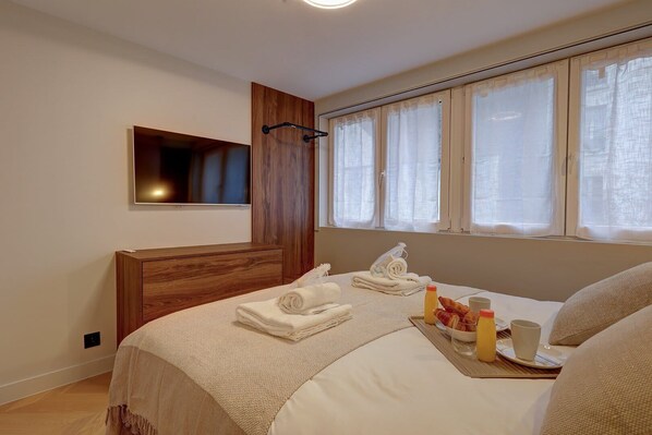 Une chambre d’hôtel avec un lit, une table de chevet avec une lampe, une fenêtre avec des rideaux et un téléviseur fixé au mur.