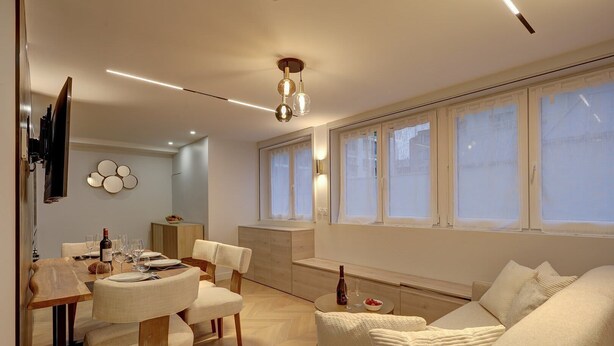 Een moderne woonkamer met een eethoek, grote ramen en een plafondlamp.