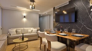 Een moderne woonkamer met een bank, een eettafel, stoelen, een tv die aan een marmeren muur is bevestigd en een plafondventilator.