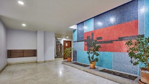 Een ruime lobby met een betegelde muur, een houten bank en potplanten.