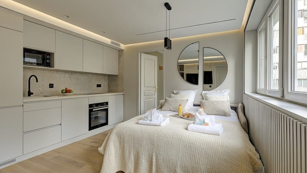 Een moderne slaapkamer met een groot bed, nachtkastjes, een inbouwkast, een keukenhoek met een magnetron en oven, en een groot raam met uitzicht.
