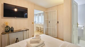 A hotel room with a bed, a TV mounted on the wall, a desk with a vase, and a view of the bathroom.