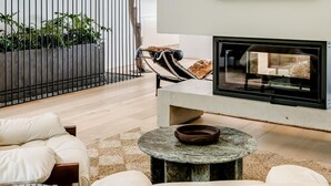 Un salón moderno con chimenea, un cuadro abstracto grande y vistas a un balcón con plantas.