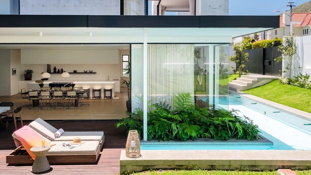 Una casa moderna con un patio con paredes de vidrio, un comedor y una piscina.