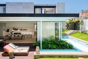 Une maison moderne dotée d’un patio entièrement vitré, d’un coin repas et d’une piscine.