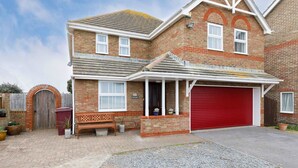 A two-story brick house with a red garage door, a wooden bench, and a brick wall with a window. - Spacious 4-bed Seaside Retreat in Selsey (Chichester)
