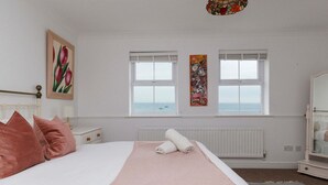 A bedroom with a bed, two windows, a radiator, and a painting on the wall. - Spacious 4-bed Seaside Retreat in Selsey (Chichester)
