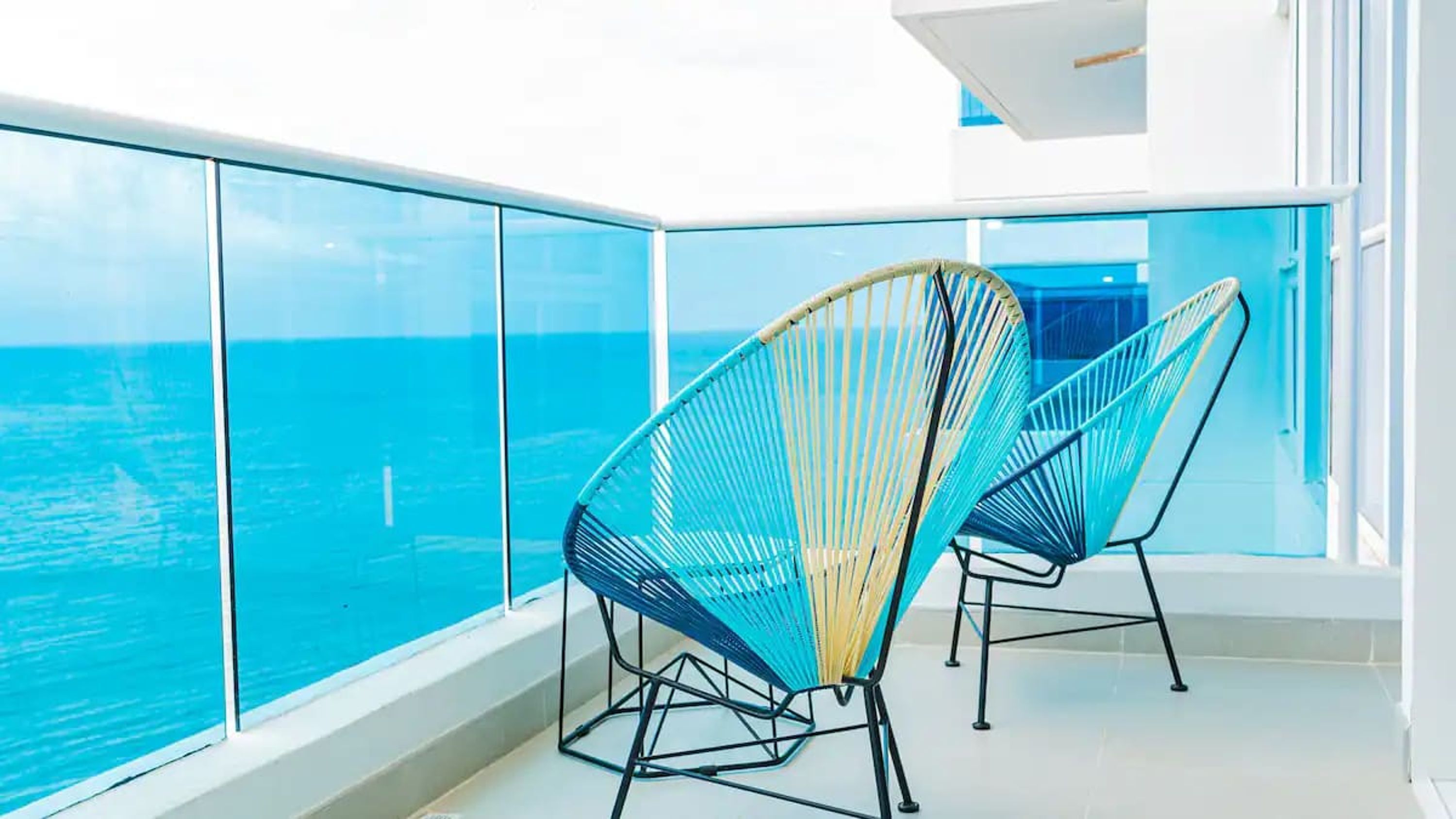 Un balcon doté de rampes en verre donnant sur l’océan, avec deux fauteuils de relaxation bleus et jaunes.