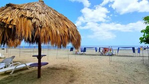 A beach with a thatched umbrella, lounge chairs, and a blue tent. - Majestic 3BR With Fantastic Pool in Bolivar (Santa Marta)