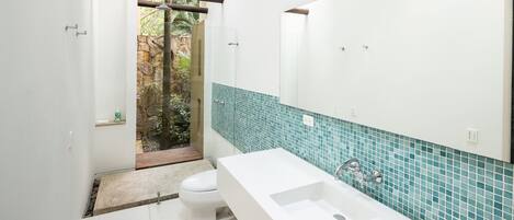 A modern bathroom with a white sink, a large mirror, and a view of a garden through a glass door.