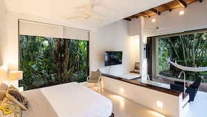 A modern bedroom with a large bed, a desk, and a TV. There are large windows with a view of greenery. - w Splendid 5BR Villa at Mesa de Yeguas (Anapoima)